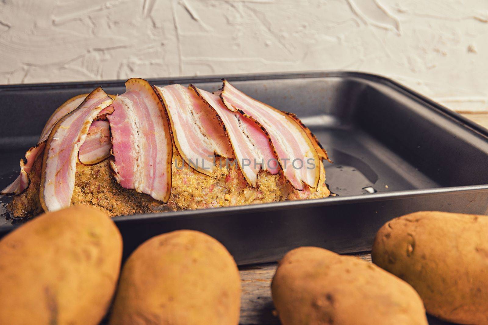 Meat loaf with slices of bacon. Home-made meat loaf on roasting pan. Potatoes foregraund