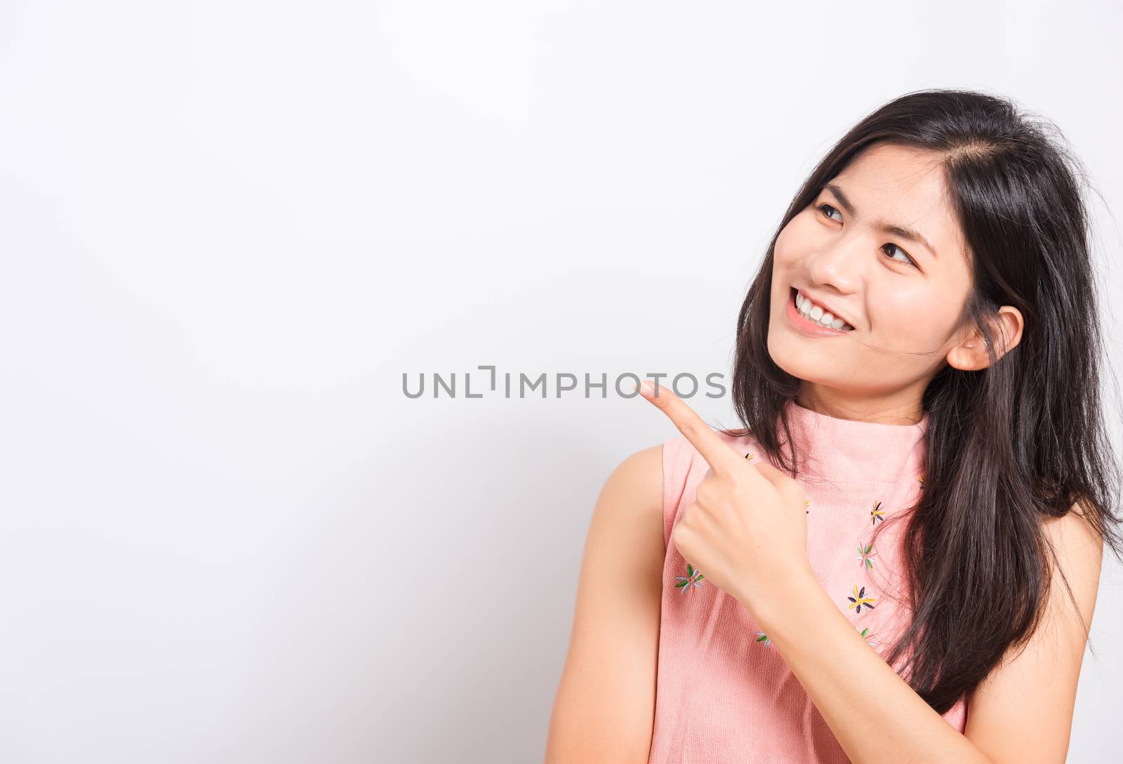 Portrait Asian beautiful young woman standing smile seeing white teeth, She pointing finger up and looking at side, shoot photo in studio on white background. There was copy space to put text