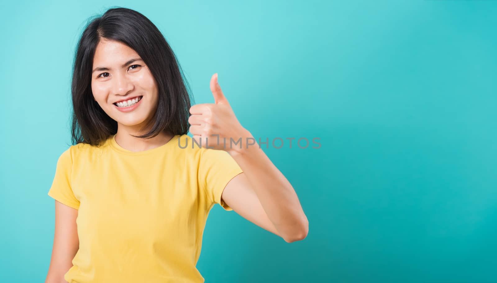 Portrait Asian beautiful young woman standing, She made finger thumbs up, Ok sign to agree and looking at camera, shoot photo in studio on blue background, There was copy space