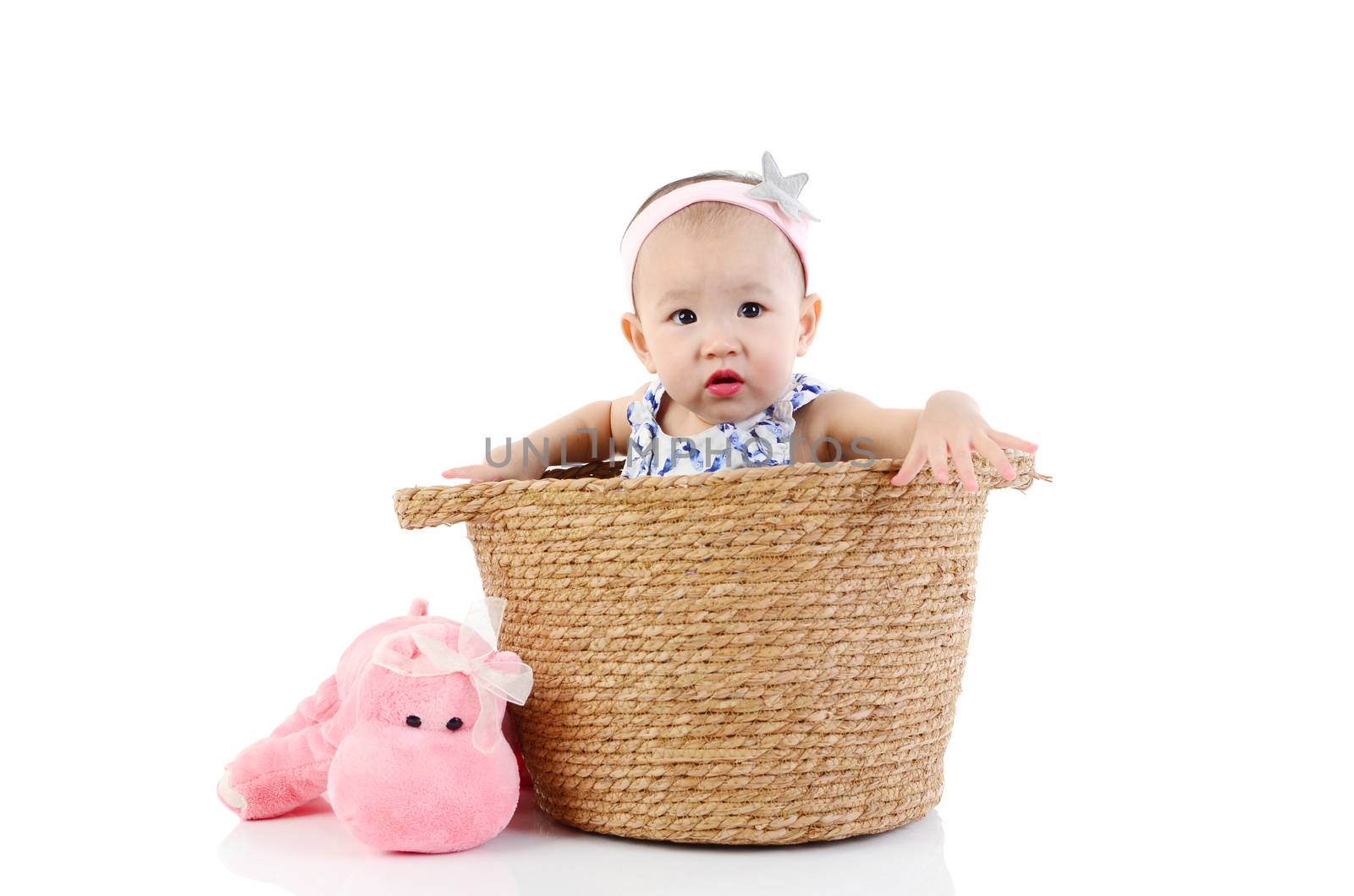 Cute asian girl sitting inside basket on the floor and playing toy