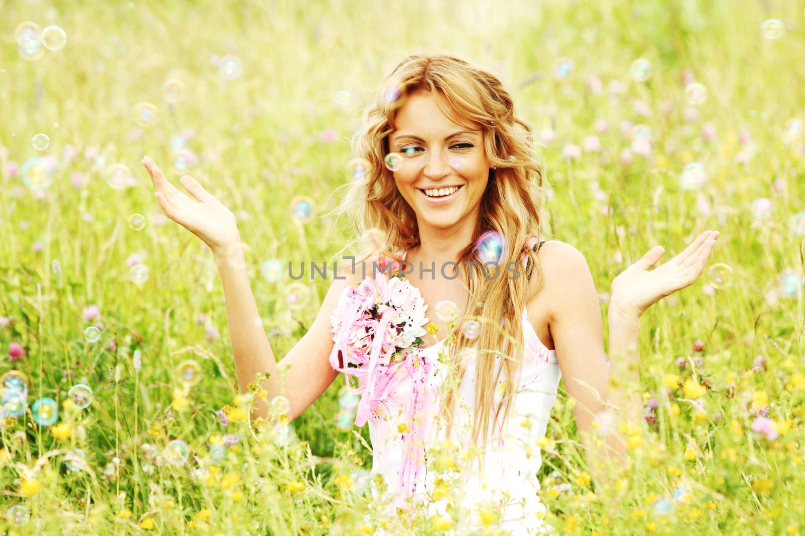 Blonde girl starts soap bubbles and smiling in a green spring field