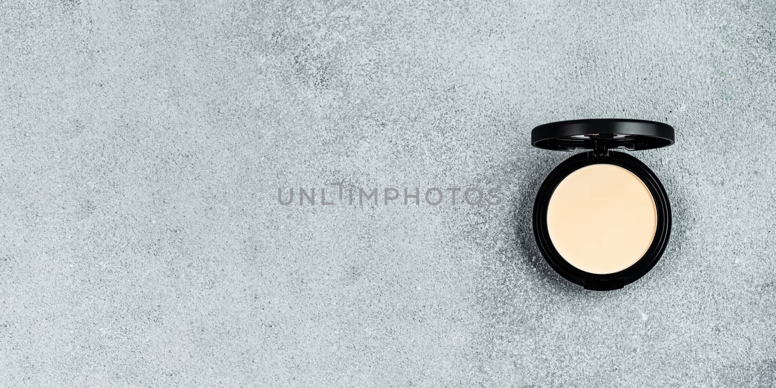 Compact powder on gray cement background. Female pressed powder in opened black plastic case with mirror, copy space for text or design. Top view or flat lay. Long horizontal banner