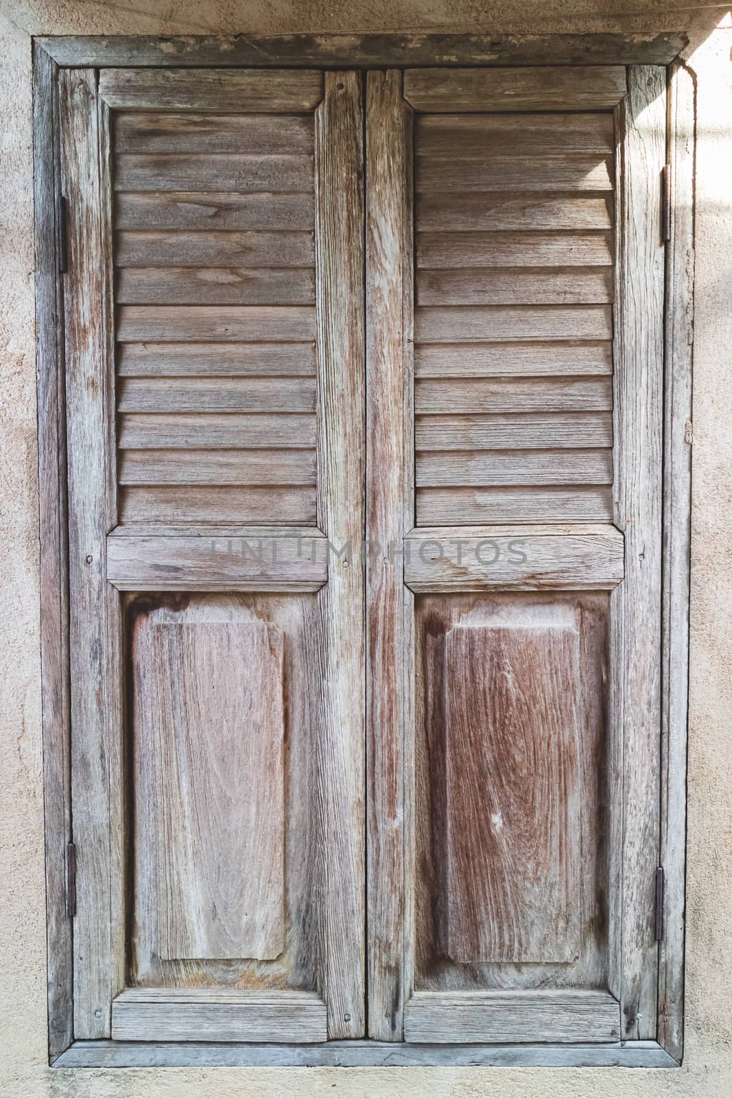 An old, shuttered wooden window with morning sunlight shining from the side on the cement wall in an old house.