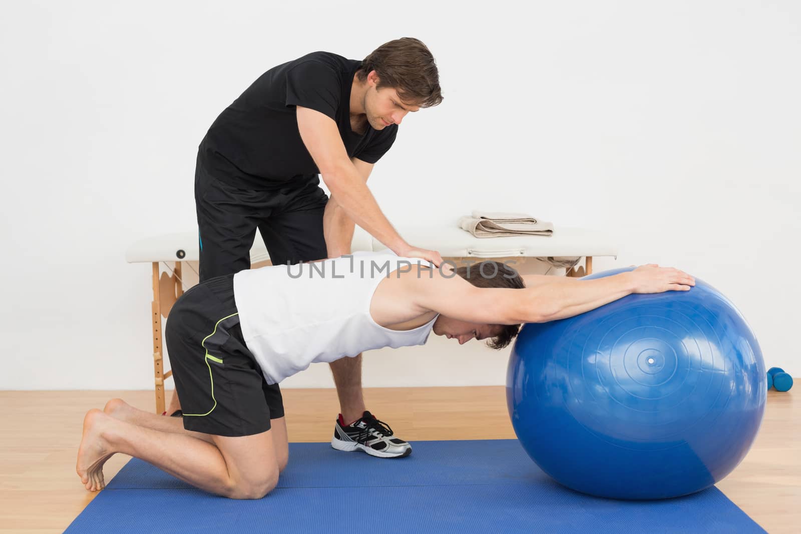 Physical therapist assisting young man with yoga ball by Wavebreakmedia