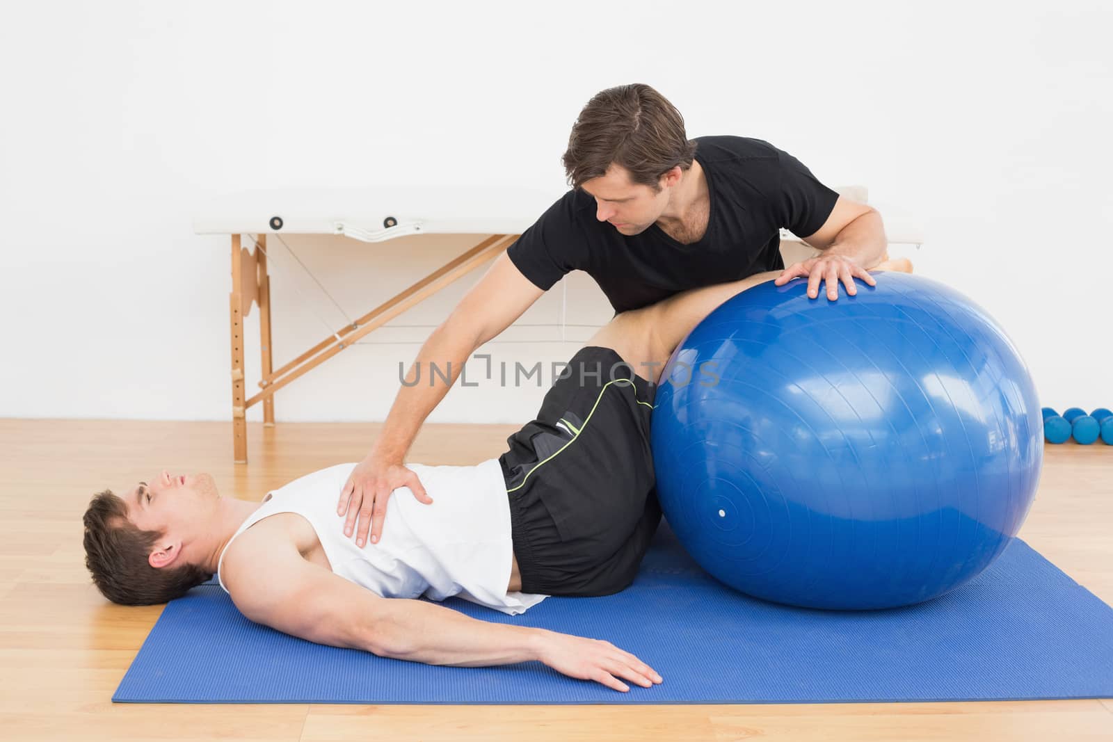 Physical therapist assisting young man with yoga ball by Wavebreakmedia