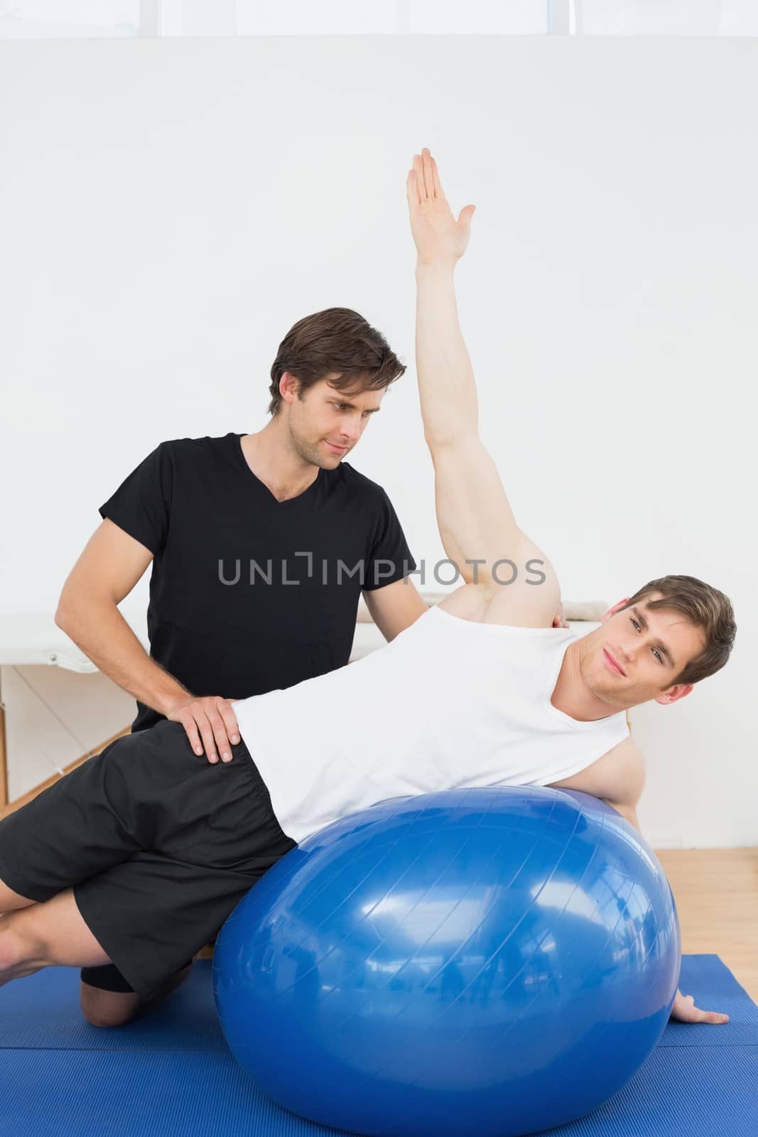 Physical therapist assisting young man with yoga ball in the gym at hospital