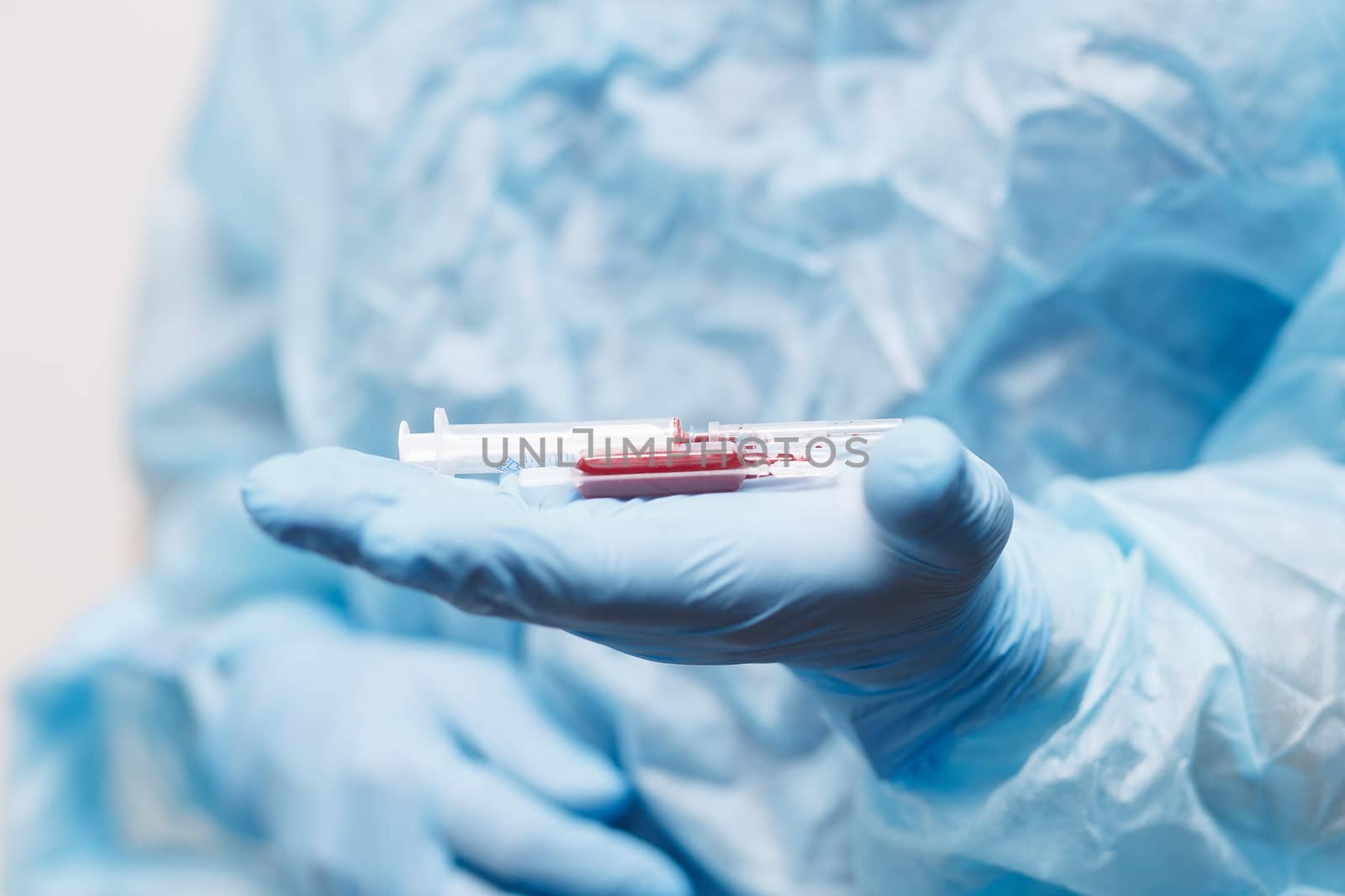 Close up of doctor hand holding syringe and blood sample. Medical equipment. Blood test. A doctor wearing personal protective equipment including mask, goggle, and suit to protect COVID 19 coronavirus infection.