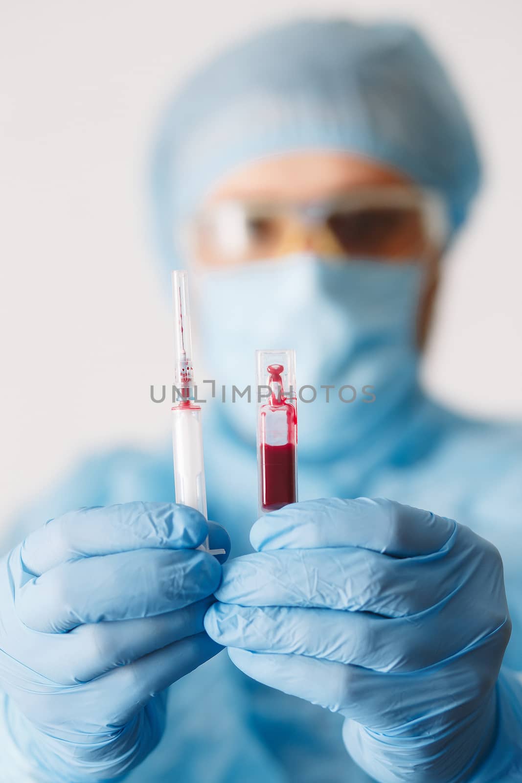 Close up of doctor hand holding syringe and blood sample. Medical equipment. Blood test. A doctor wearing personal protective equipment including mask, goggle, and suit to protect COVID 19 coronavirus infection.