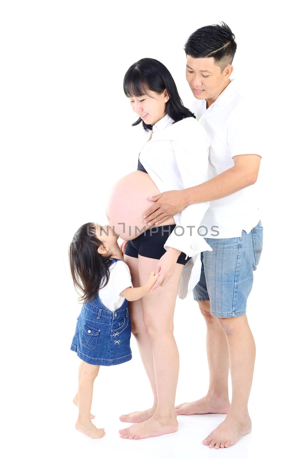 Little asian girl kissing her pregnant mother belly and smiles at home