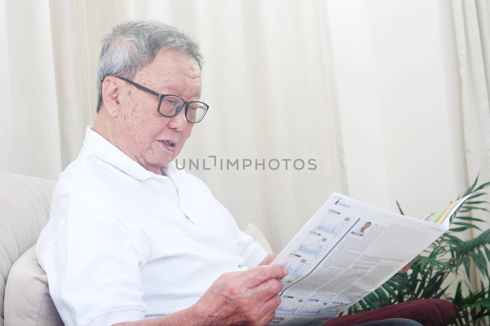 Asian senior man reading newspaper at home