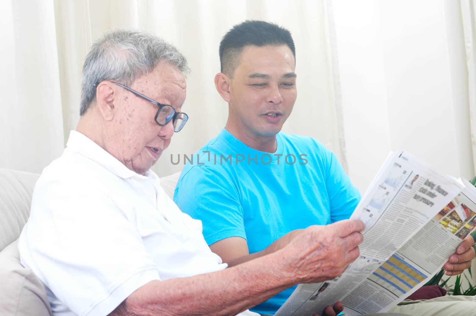 Portrait of chinese family reading newspaper together at home. Mature 80s senior man and his son