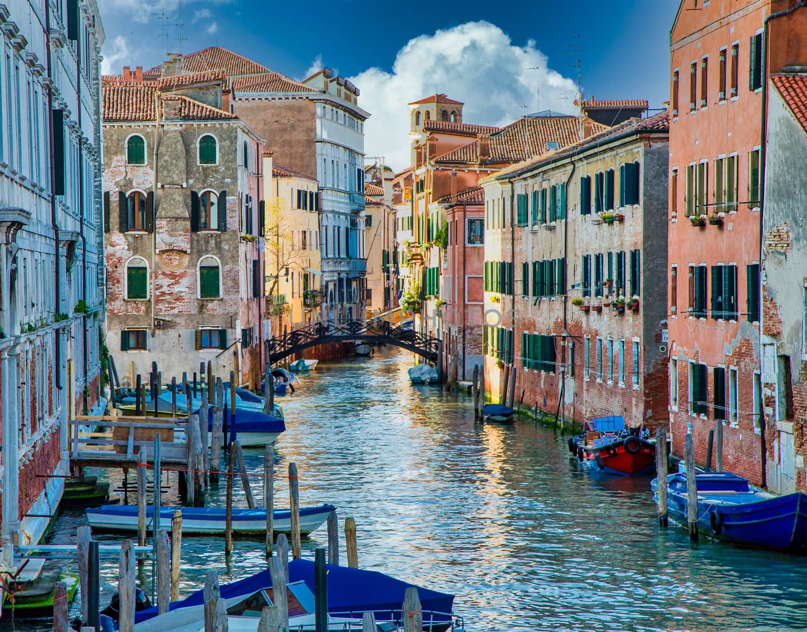 Many boats in a Venice canal with black iron bridge