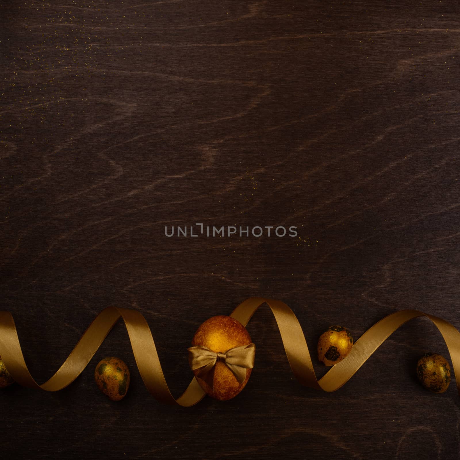 Golden luxury easter eggs and ribbon composition on dark wooden background with copy space for text card