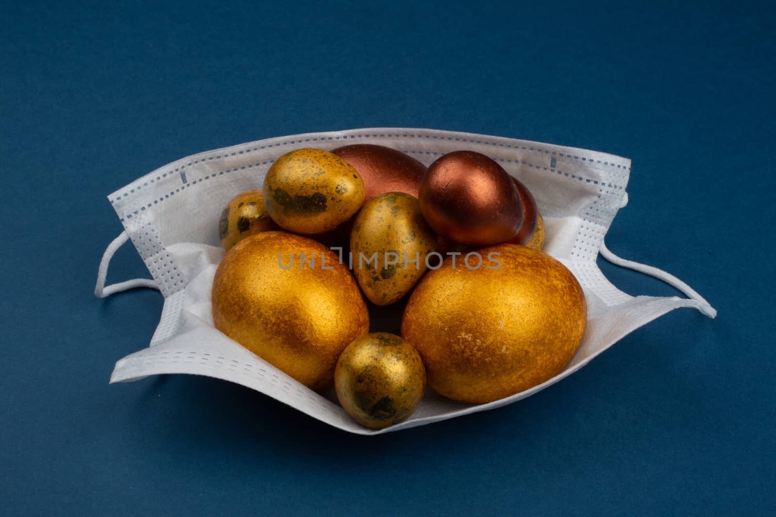 Easter 2020 conceptual image with golden easter eggs in protective medical mask. Cancellation of celebration concept coronavirus pandemic. Antiviral mask. COVID quarantine. Protection from virus COVID-19