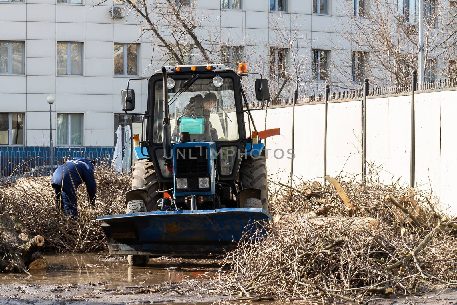 The city improvement service conducts spring cleaning of the city in Moscow. The tractor collects and disposes of cut tree branches. The worker got out of the car.