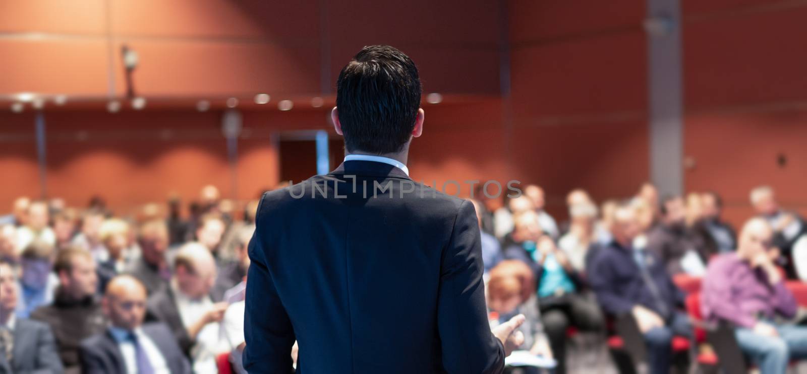 Speaker giving a talk on corporate business conference. Unrecognizable people in audience at conference hall. Business and Entrepreneurship event.