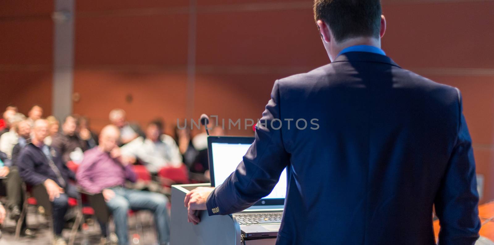 Speaker giving a talk on corporate business conference. Unrecognizable people in audience at conference hall. Business and Entrepreneurship event.