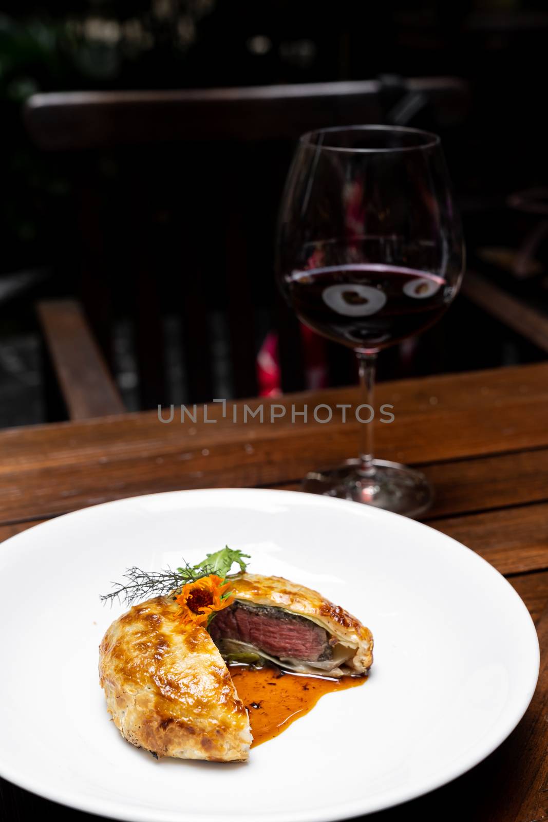 Roasted Beef Wellington with gravy brown savory sauce, international gourmet cuisine of stuff beef meat in baked bread puff with glass of red wine. Unising for recipe menu pf food and drink industry.