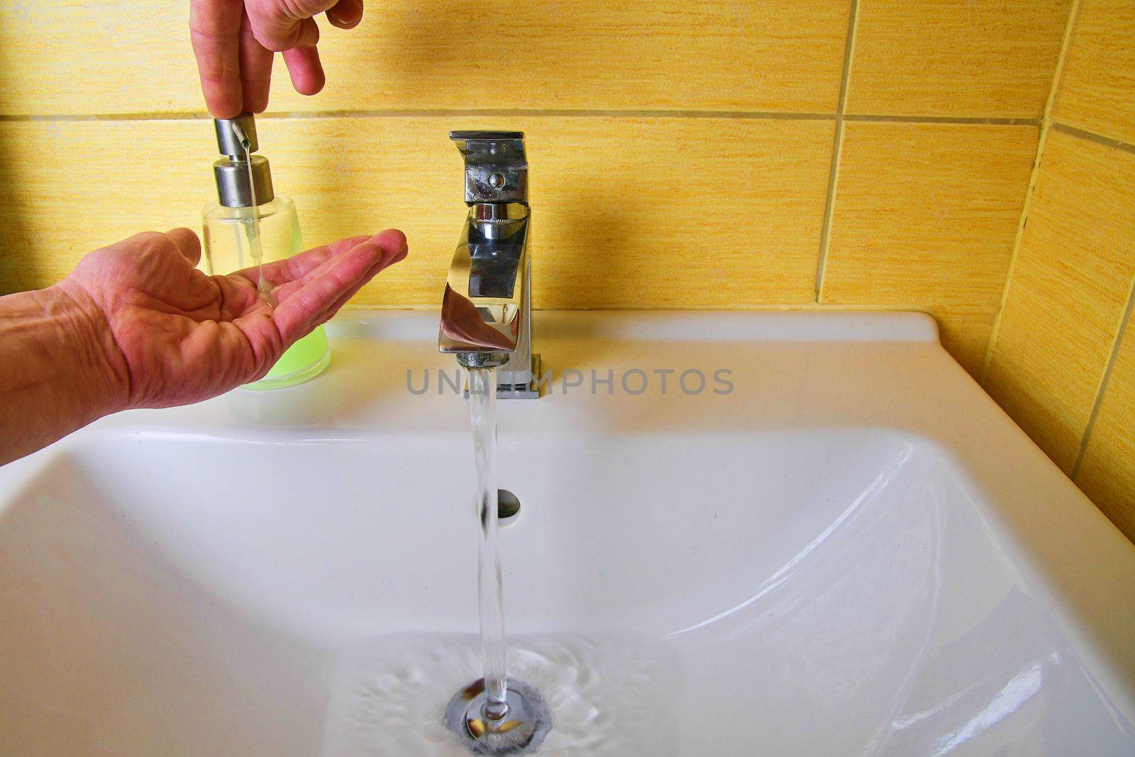 Closeup of a caucasian man washing his hands with soap in the sink of a bathroom. Prevention of spreading coronavirus. Covid 19