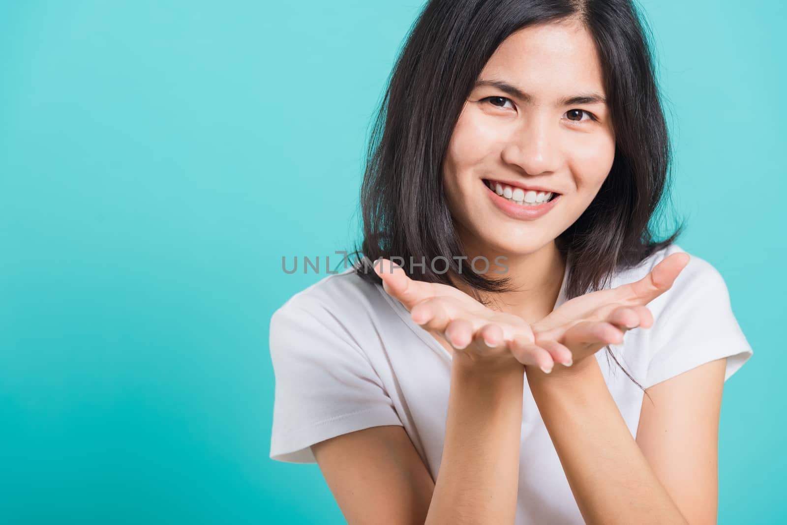 Portrait happy Asian beautiful young woman smile standing wear a white t-shirt, She blowing air kiss something on palms, studio shot on blue background with copy space for text