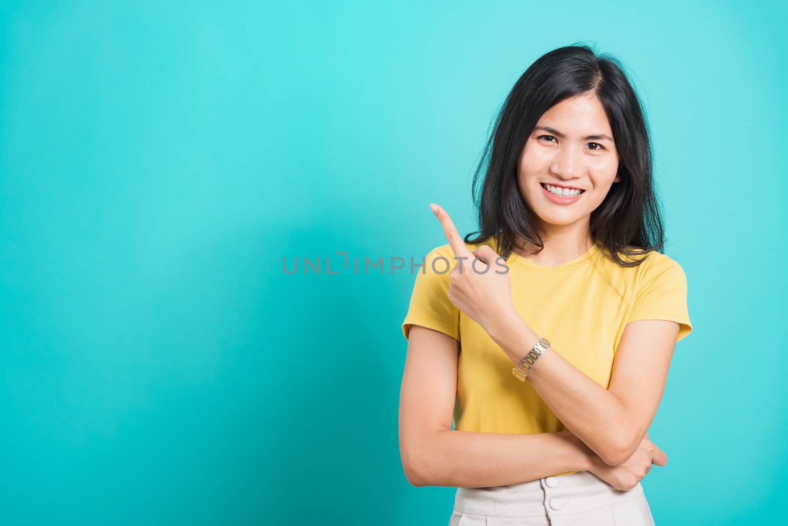 Portrait Asian beautiful young woman wearing yellow T-shirt standing smile white teeth, She pointing finger up and looking at camera, shoot photo in studio on blue background, There was copy space.