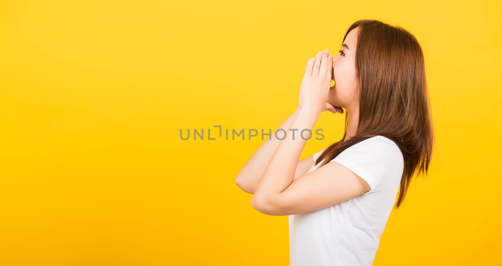 Asian happy portrait beautiful cute young woman teen standing big shout out with hands next mouth giving excited positive looking to side isolated, studio shot on yellow background with copy space