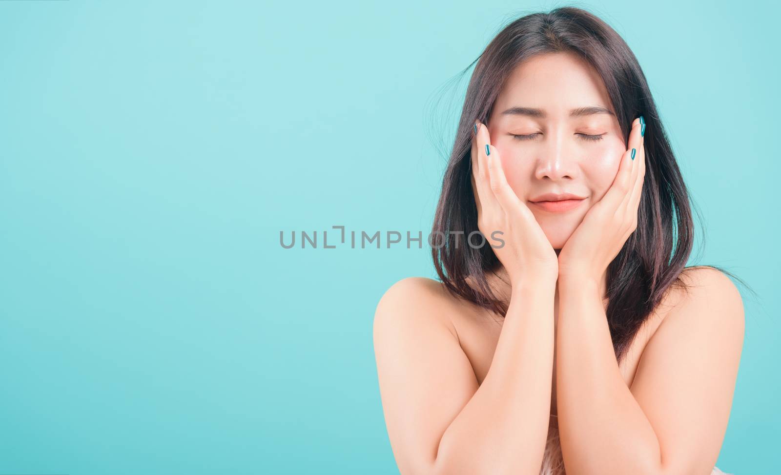 Asian happy portrait beautiful young woman standing smiling surprised excited her hands over her face and looking to camera on blue background with banner copy space for text