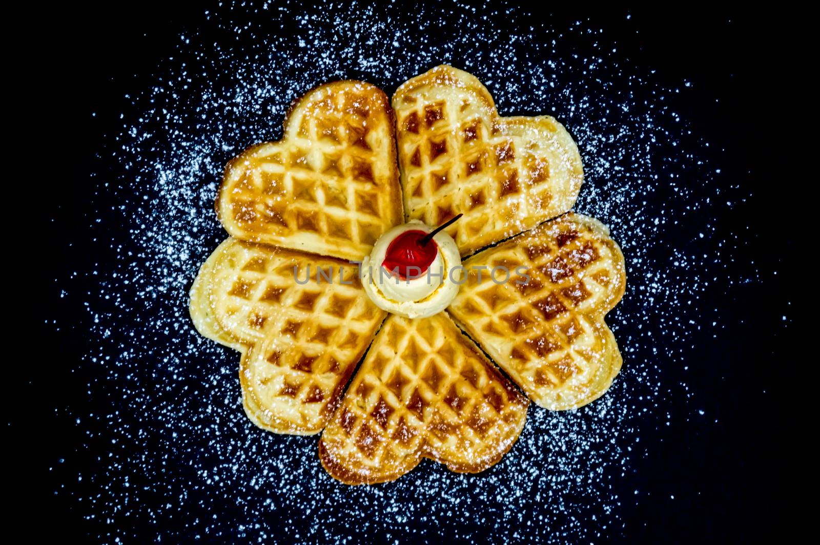 Homemade waffles with powdered sugar, a scoop of vanilla ice cream and a cherry on a black background, isolated image of food.