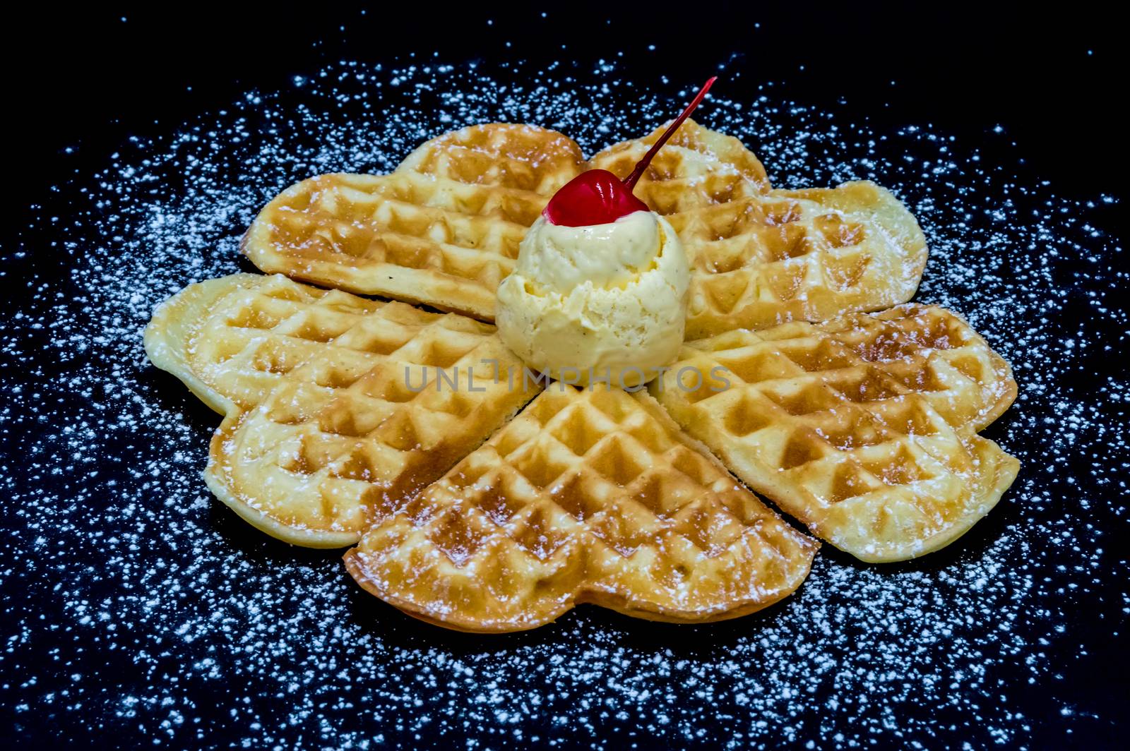 Homemade waffles with powdered sugar, a scoop of vanilla ice cream and a cherry on a black background, isolated image of food.