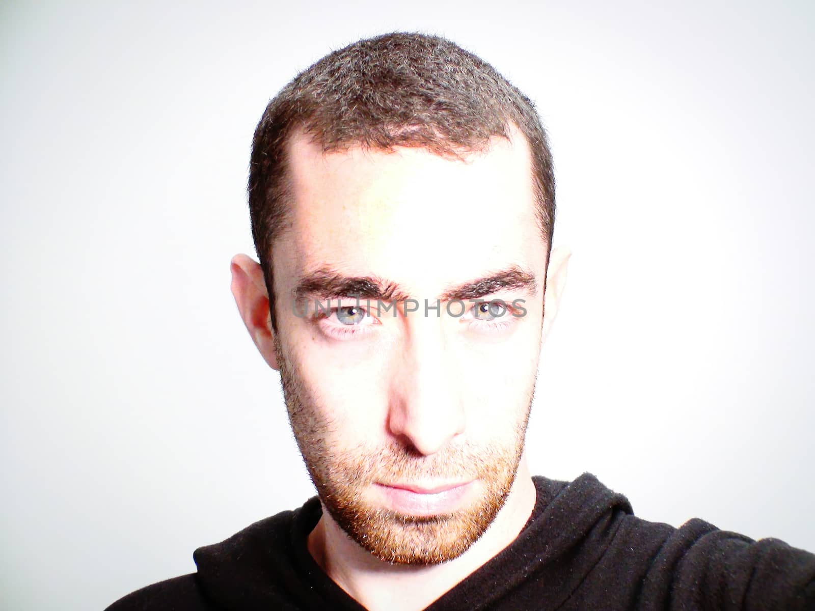 Bearded man with serious facial expression with glow light on his face looking at the camera. Close up portrait of an expressionless young man on white background.