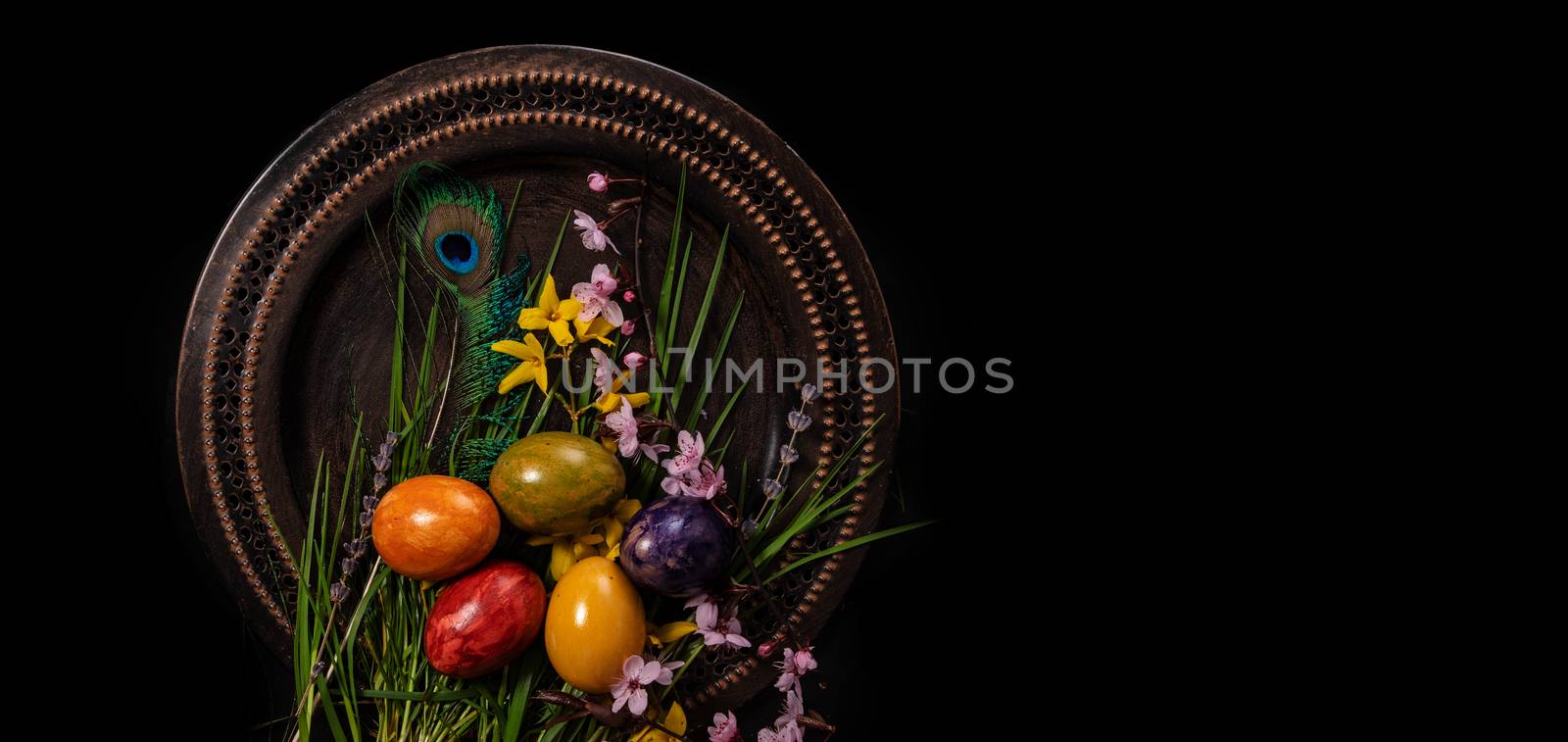 Colored easter Eggs in a plate with black background and copy space. With grass and flowers