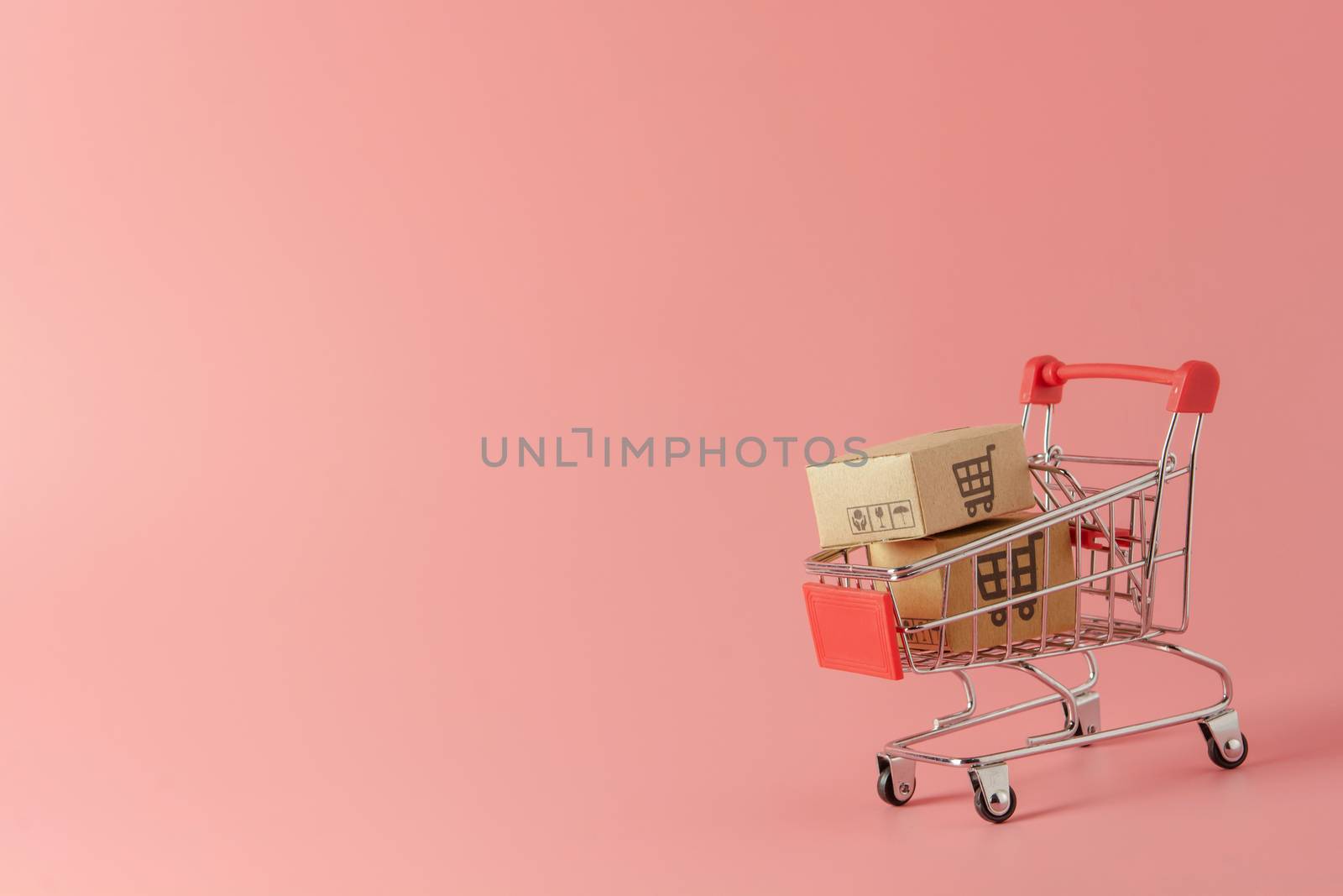 Shopping concept : Cartons or Paper boxes in red shopping cart on pink background. online shopping consumers can shop from home and delivery service. with copy space