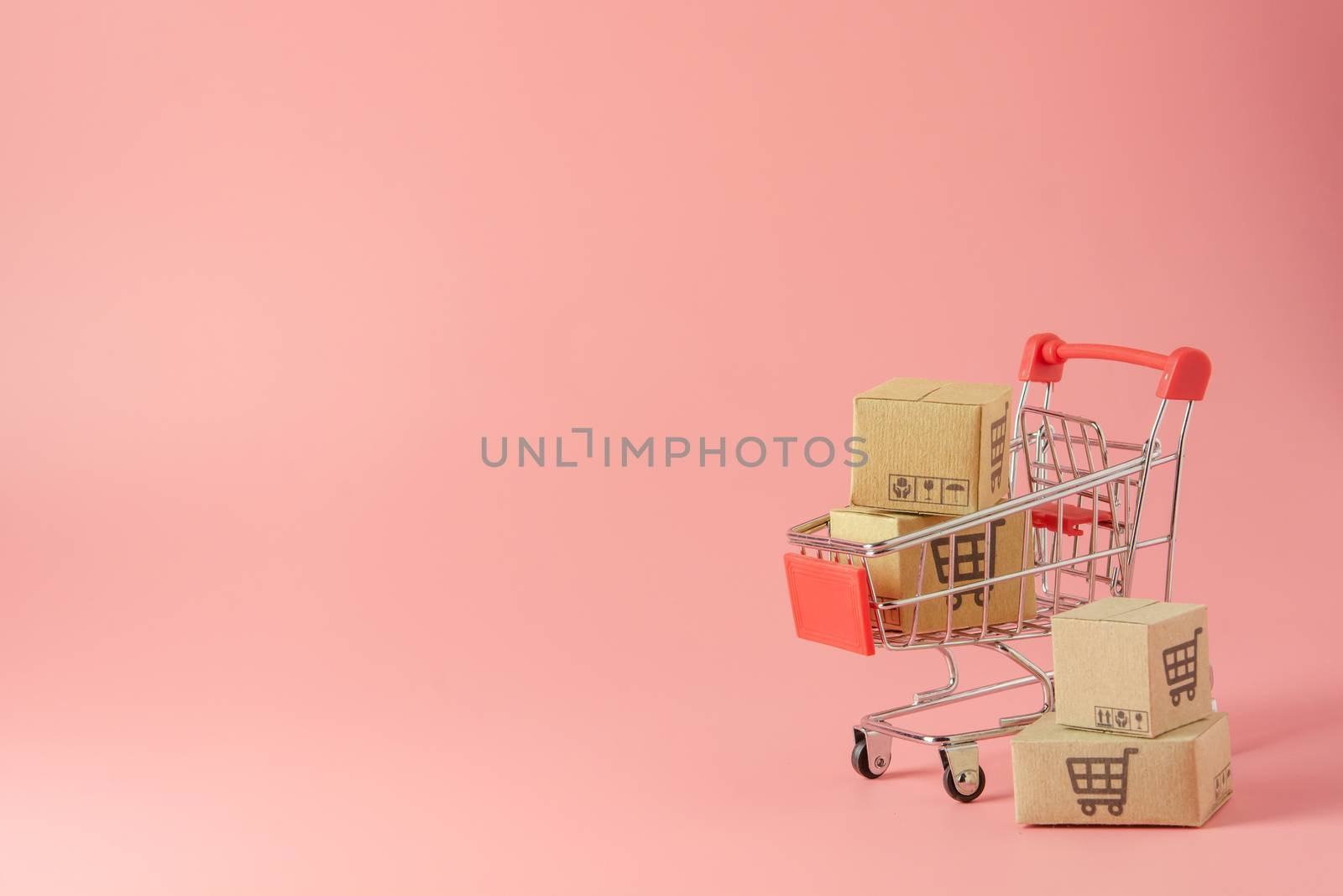 Shopping concept : Cartons or Paper boxes in red shopping cart on pink background. online shopping consumers can shop from home and delivery service. with copy space