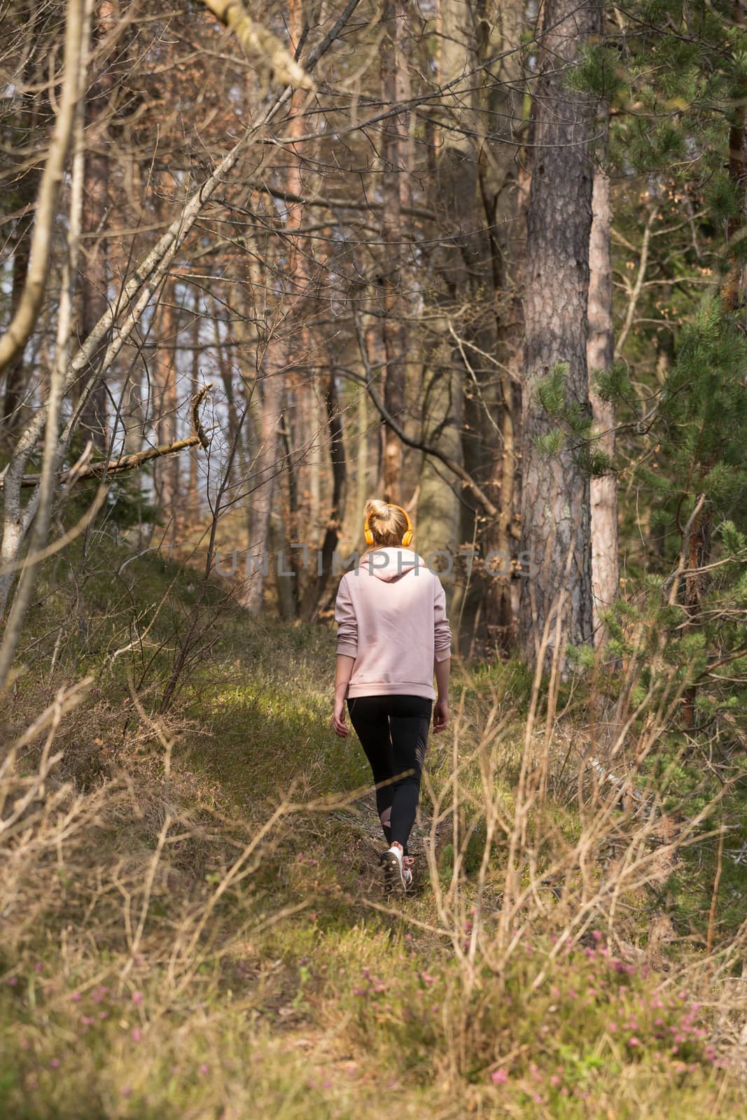 Rear view of active sporty woman listening to the music while running in autumn fall forest. Female runner training outdoor. Healthy lifestyle image of young caucasian woman jogging outside.