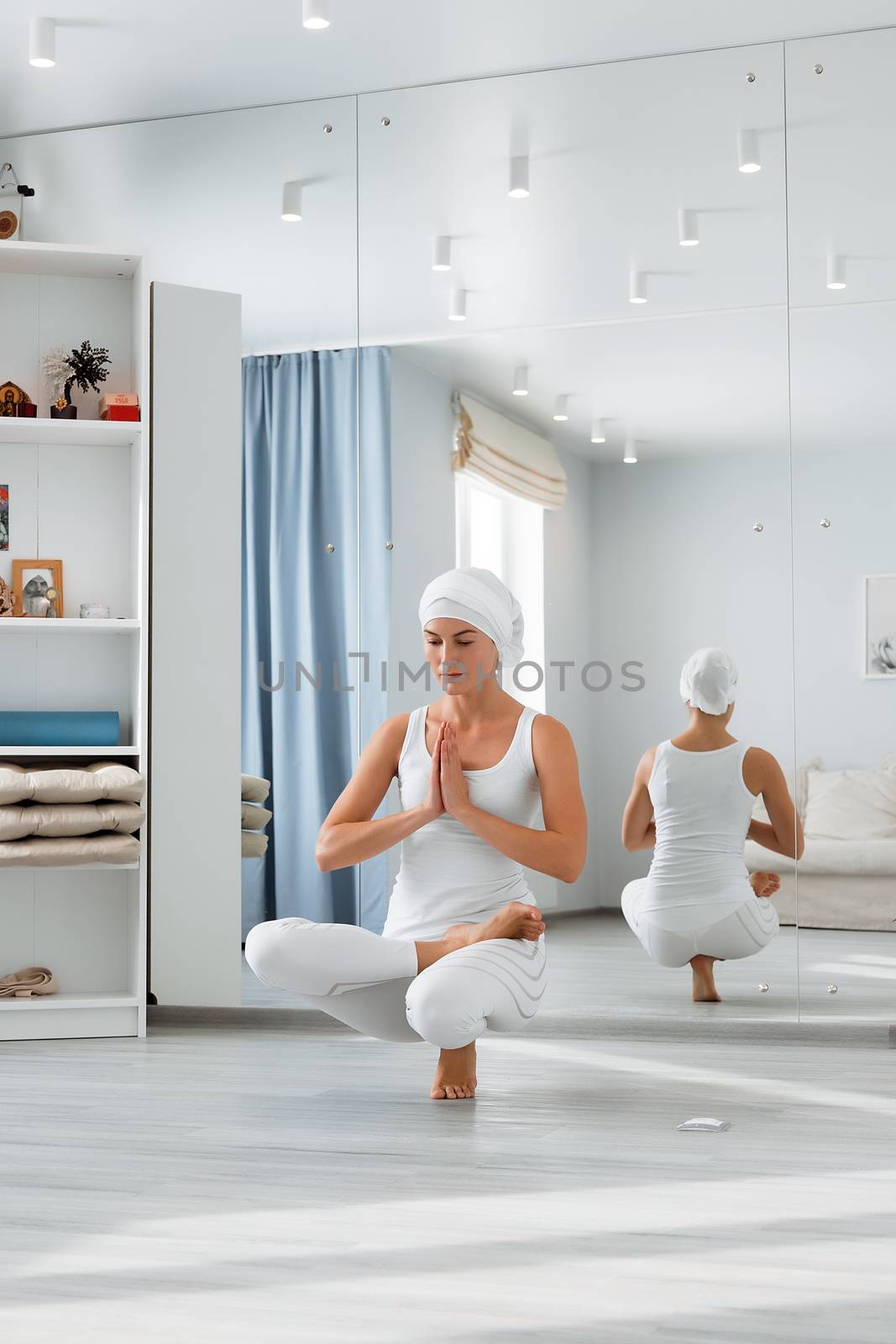 Pretty young woman in sportswear sitting on studio floor in difficult position while doing yoga