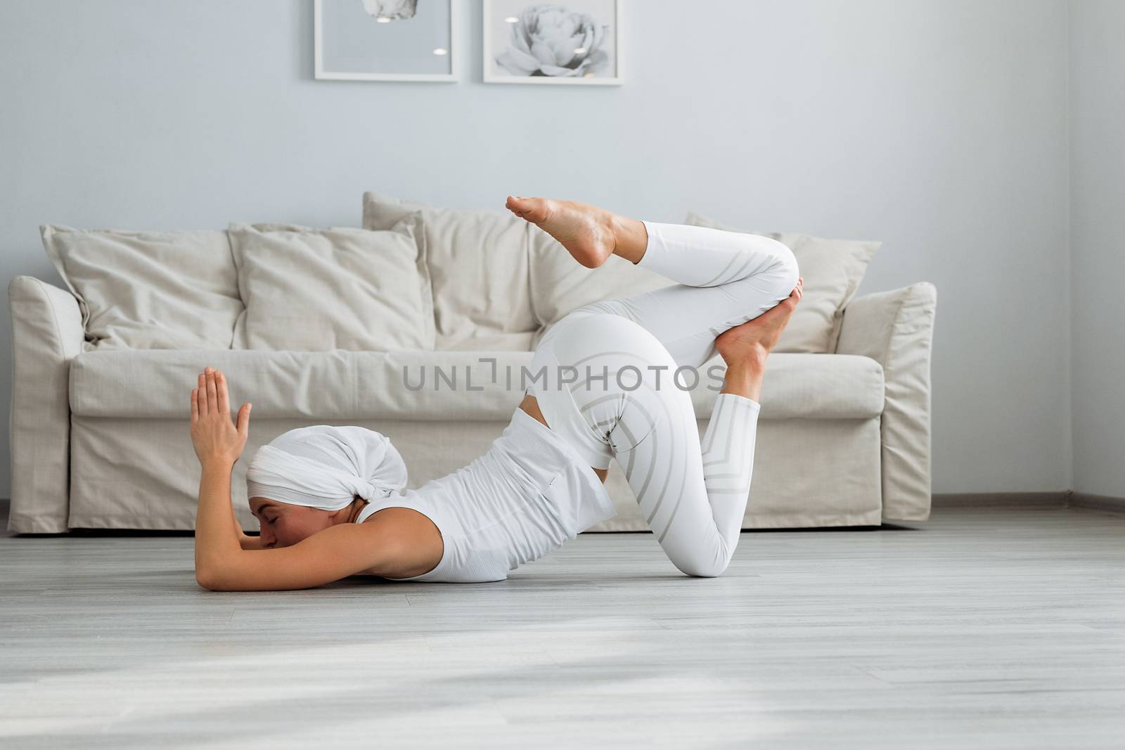Pretty young woman in sportswear sitting on studio floor in difficult position while doing yoga