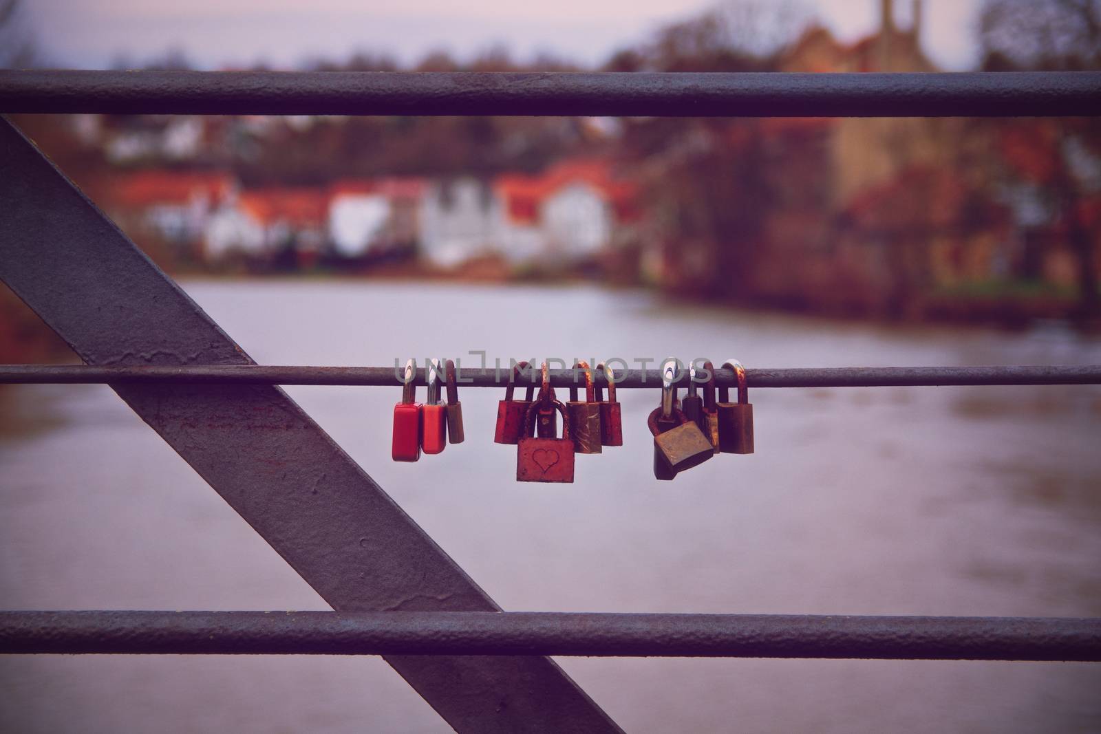 Lovelocks hanging on a bridge railing with a river in the background. Romantic lover padlocks on a bridge in a symmetric row. Symbol of unbreakable love and lifetime commitment for couples. Love, marriage, relationship concept.