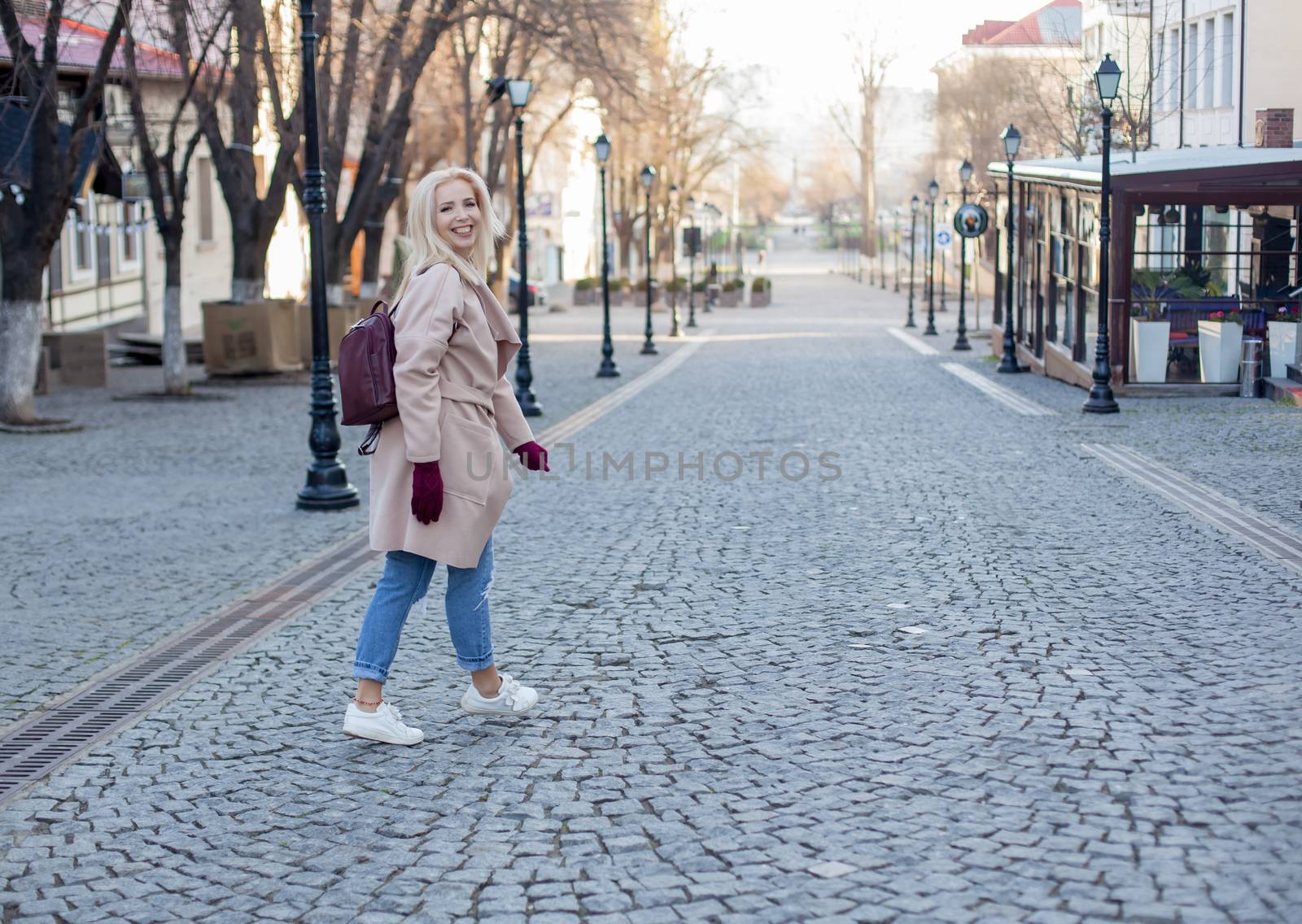 Outdoor of gorgeous woman with blond hair in elegant coat and gloves walking in street