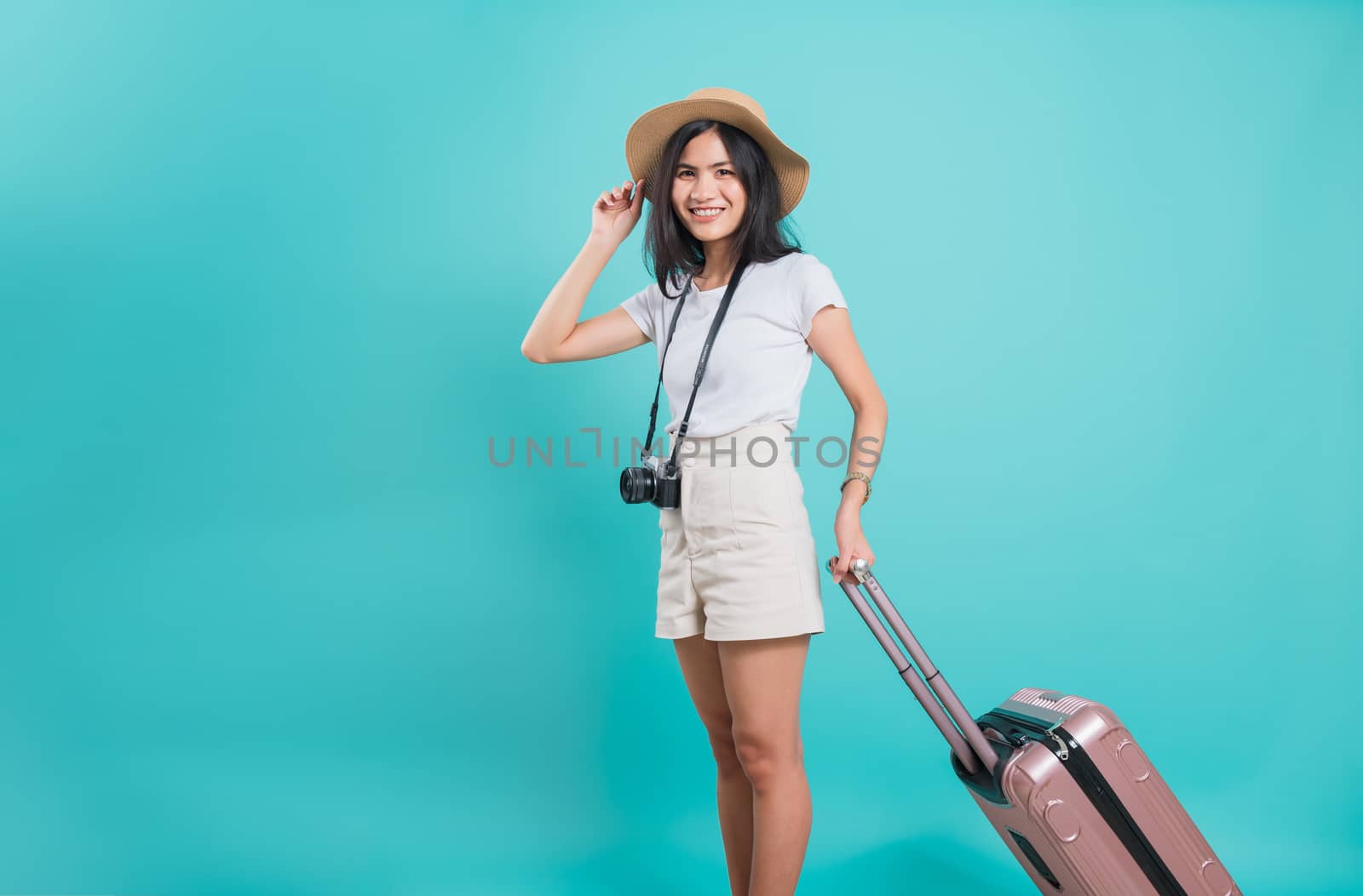 Traveler tourist happy Asian beautiful young woman standing wear white t-shirt, holidays travel concept, her holding suitcase bag and photo mirrorless camera, shoot photo in studio on blue background