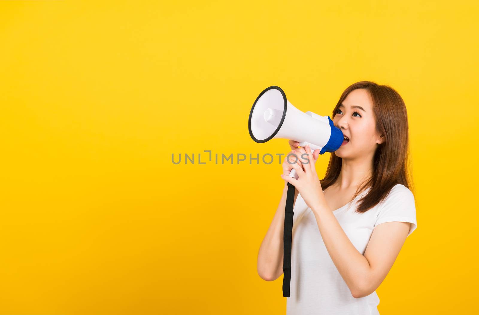 Asian happy portrait beautiful cute young woman teen standing making announcement message shouting screaming in megaphone looking to side isolated, studio shot on yellow background with copy space