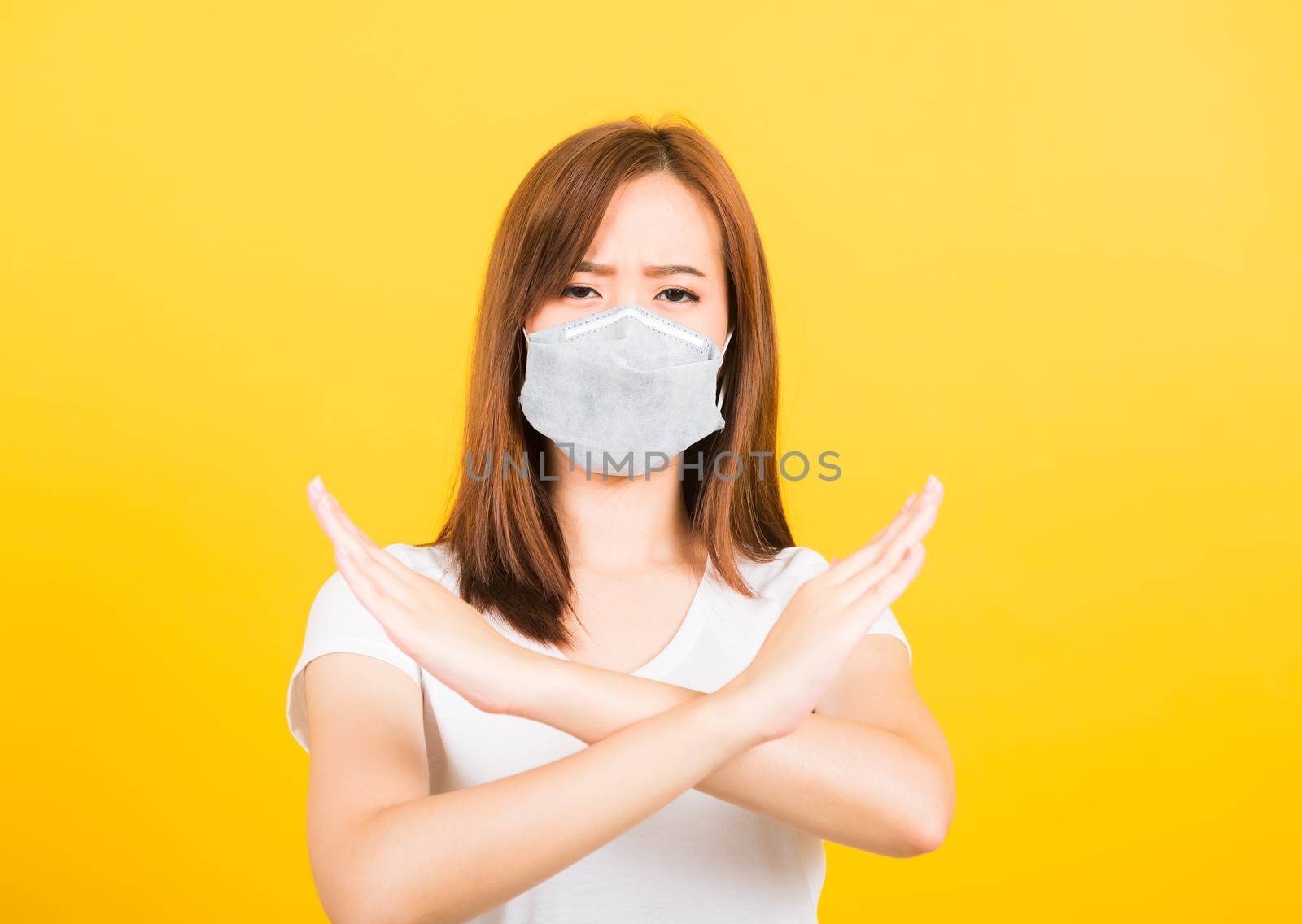 Portrait Asian beautiful happy young woman wearing face mask protects filter dust pm2.5 anti-pollution, anti-smog, and air pollution her crossed arms show X sign on yellow background, with copy space