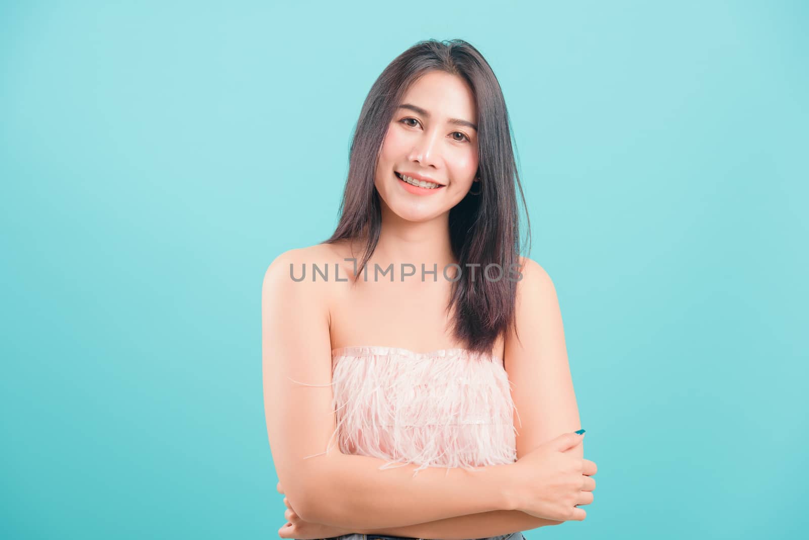 Asian happy portrait beautiful young woman standing smiling white teeth her keeping arms crossed and looking to camera on blue background with copy space for text