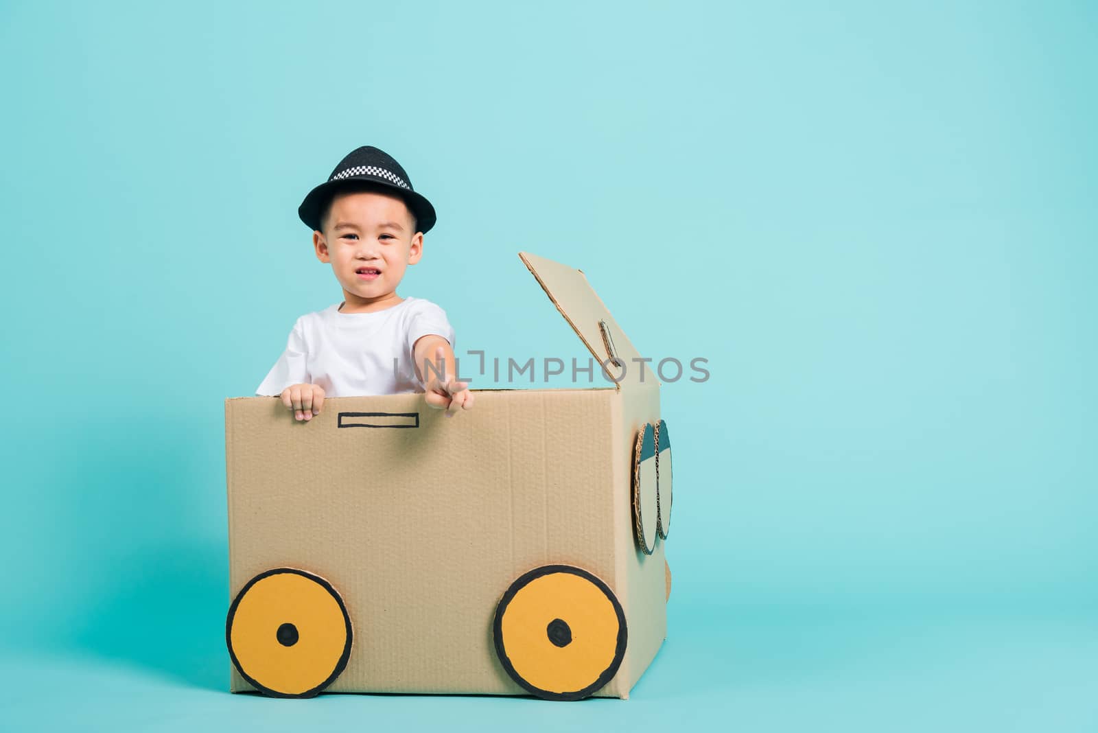 Happy Asian children boy smile in driving play car creative by a cardboard box imagination, summer holiday travel concept, studio shot on blue background with copy space for text