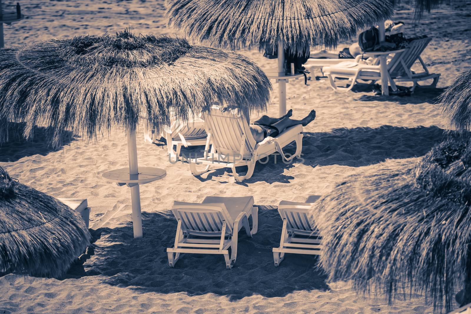 Straw umbrellas and benches on beach by Nanisimova