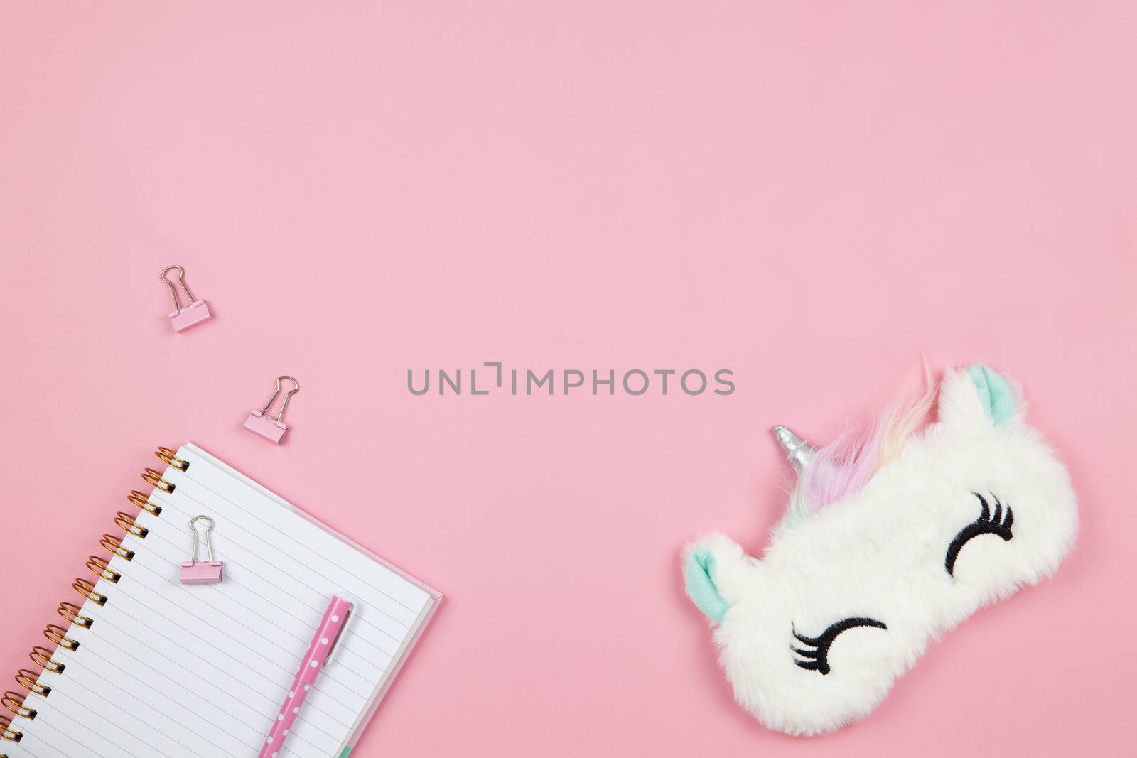 Modern female working space, top view. Cute women's or girls things, sleep mask unicorn, notepad, pen, clamps on pink backround, copy space, flat lay. Work from home concept. For blog. Horizontal by ALLUNEED