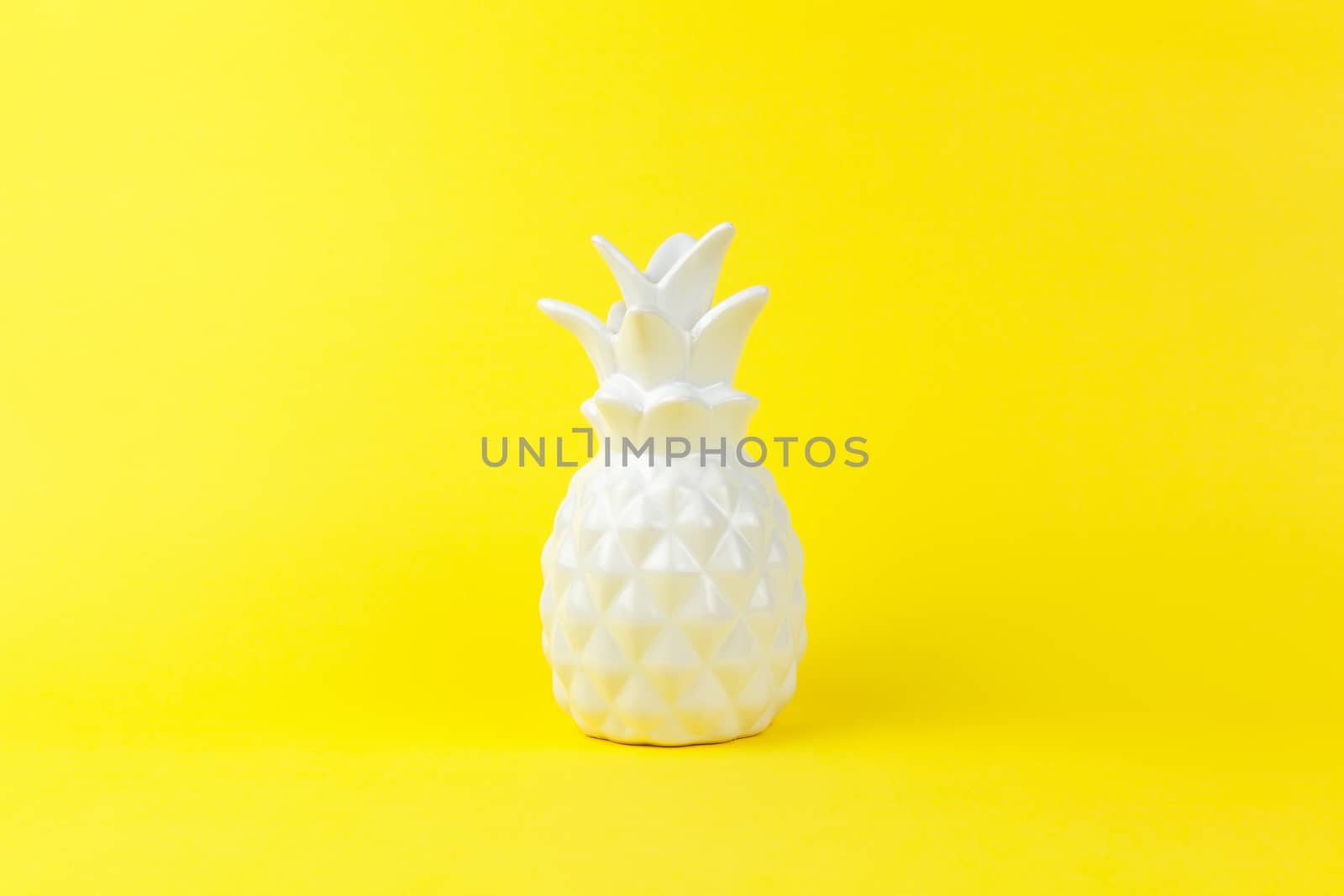 Trendy piece of interior white glossy ceramic pineapple on yellow paper background, copy space. Minimal style of decor concept. Horizontal. For lifestyle, interior blog, social media, poster.