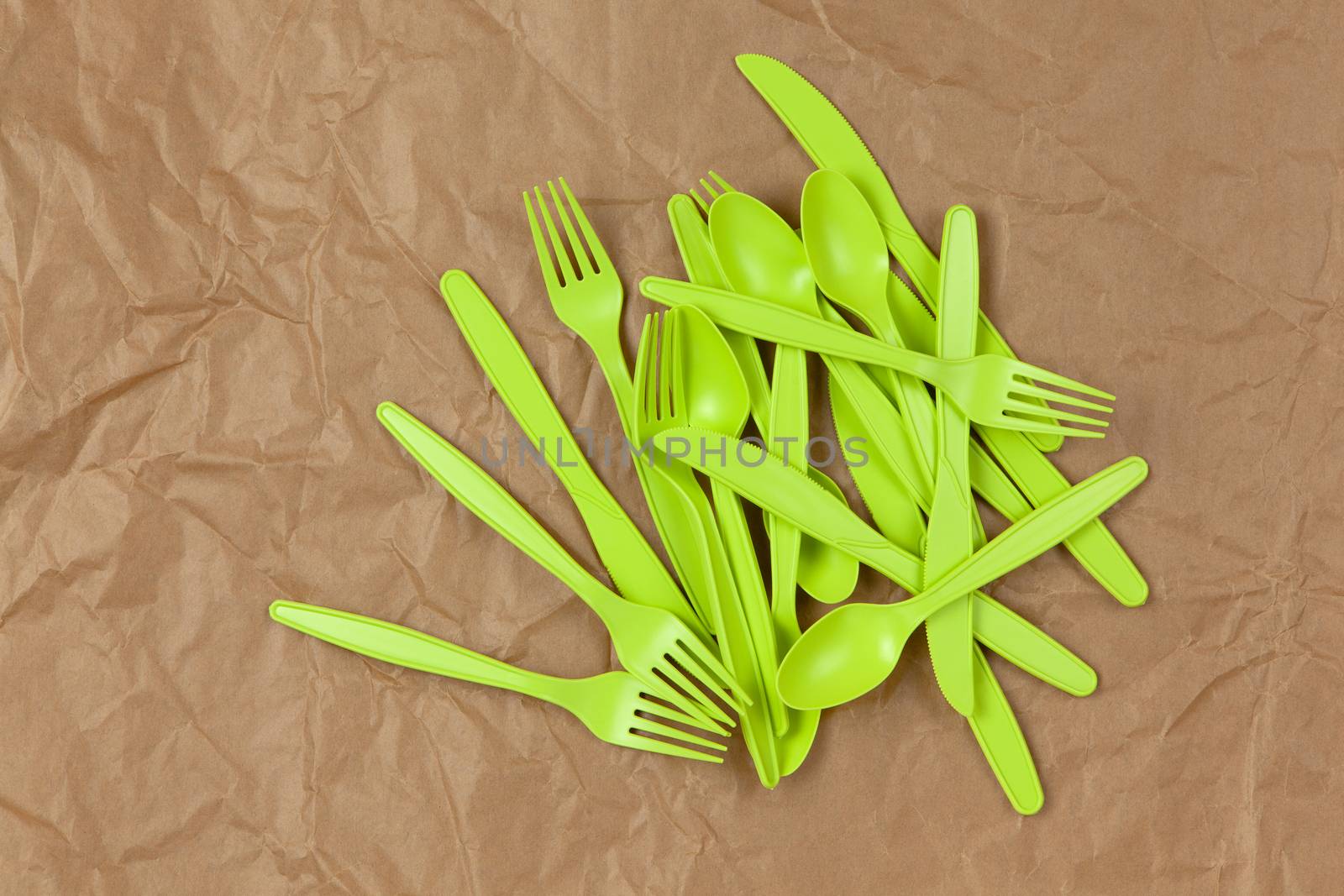 Biodegradable reusable recyclable green forks, spoons, knifes made from corn starch on brown crumpled craft paper. Eco, zero waste, alternative to plastic concept. Flat lay. Horizontal. Close-up.