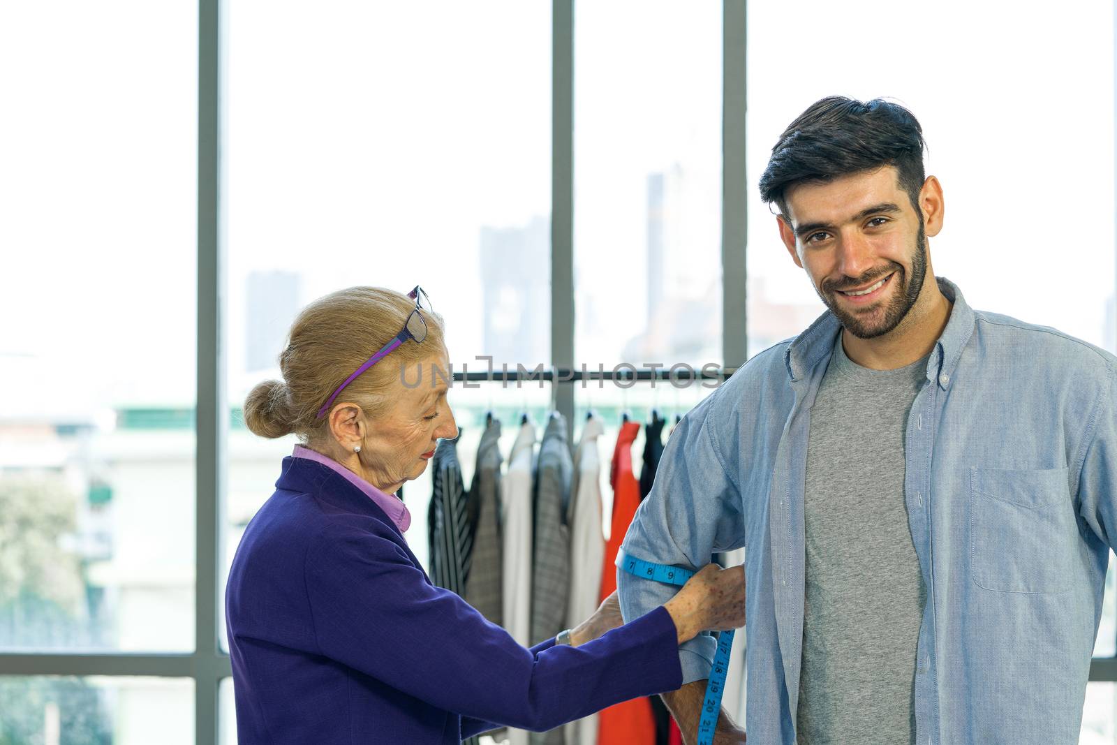 Man and woman working in home base cloth design business. Senior fashion designers measure the size of customers' arms. Young client is happy to have a new dress.