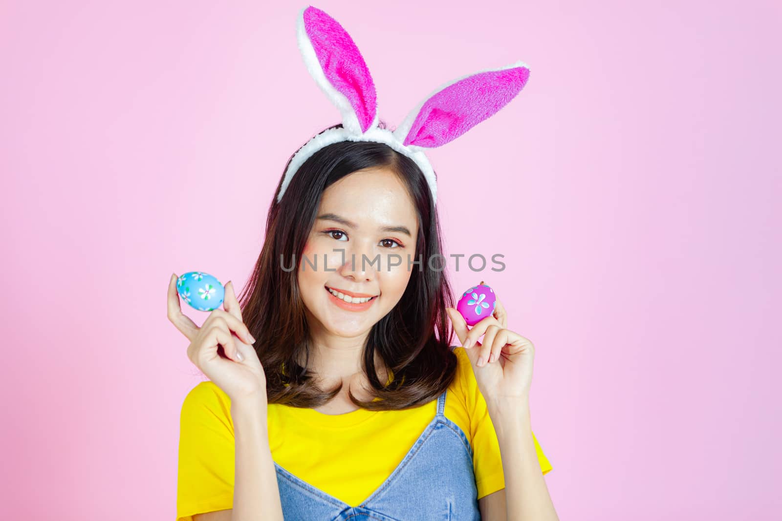 Portrait of a happy young woman wearing Easter bunny ears prepares to celebrate Easter on a pink background.