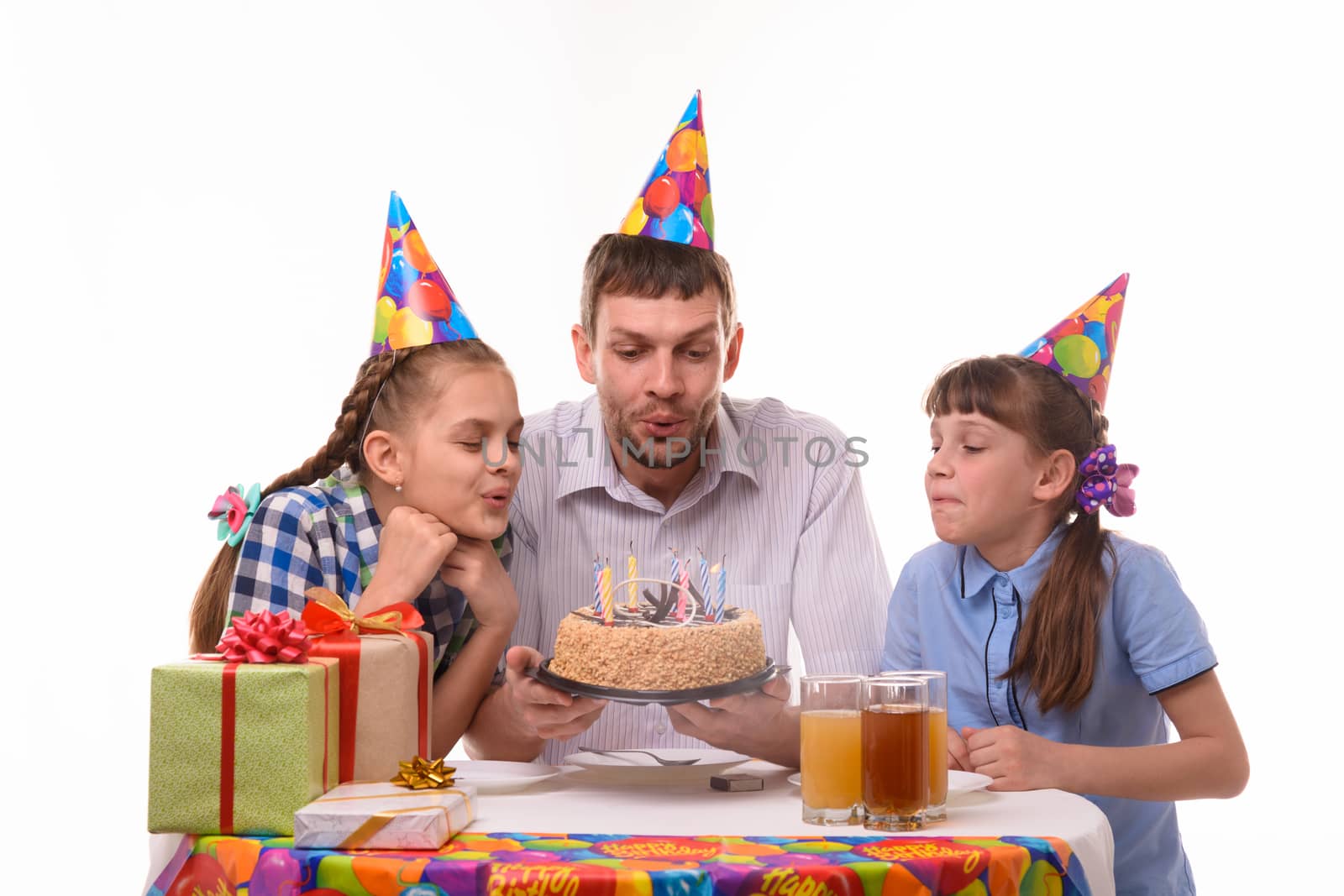 Father and two daughters blow out candles on a birthday cake